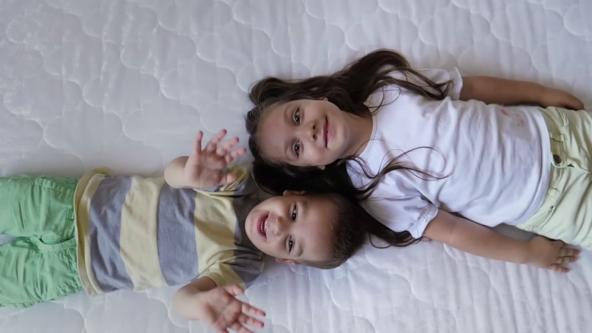 Top view portrait of happy smiling two children, sister and brother, lying head to head on the mattress in the new bedroom and having fun,waving at camera.Children friendship,happy careless childhood Royalty-Free Stock Footage #1094619711