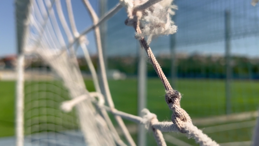 closeup of damaged soccer gate goalpost white rope net with knots and green field and blue sky in background on a windy day Royalty-Free Stock Footage #1094623243