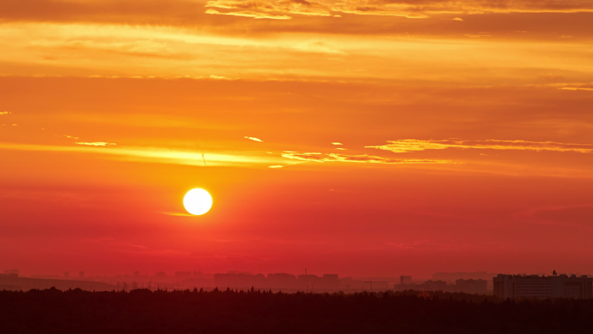 A big red sun in the sunset sky over the roofs of buildings, urban landscape. Evening sky in bright sunlight over the twilight city