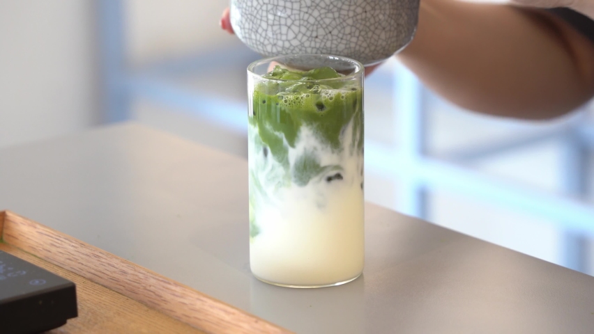 Preparation of summer refreshing beverage iced matcha latte, pouring matcha green tea mix into a glass of fresh full cream milk, cinematic close up shot. | Shutterstock HD Video #1094630391