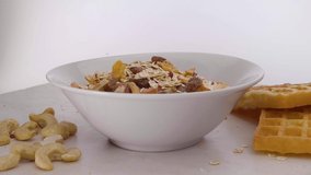 Static rotating shot of vegan muesli with various fruits and wafers with cashew nuts. Oat milk is poured into the bowl
