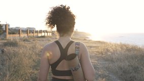 Happy curly woman strolling in summer. African American young girl going at outdoor yoga class. Beautiful mixed race young woman with yoga mat wearing sportswear walking near the seashore. Slow motion - Powered by Shutterstock - Get 15% off with code: PIKWIZARD15