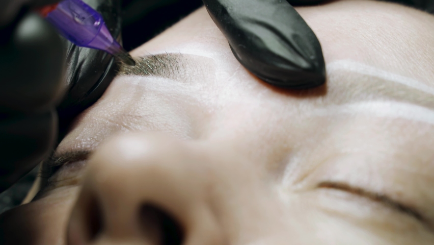 A special needle tattoo machine makes a permanent make-up correction of a woman's eyebrows. Microblading, powder coating close-up. Royalty-Free Stock Footage #1094635157