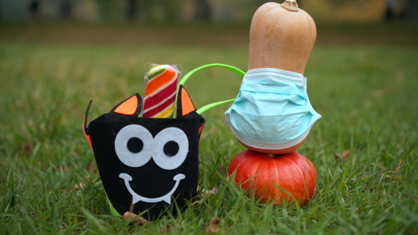 Halloween pumpkins in coronavirus face mask on green grass and female hand taking away sweet delicious lollipop from spooky basket. Unrecognizable Caucasian teen girl on All Saints Day holiday | Shutterstock HD Video #1094635409