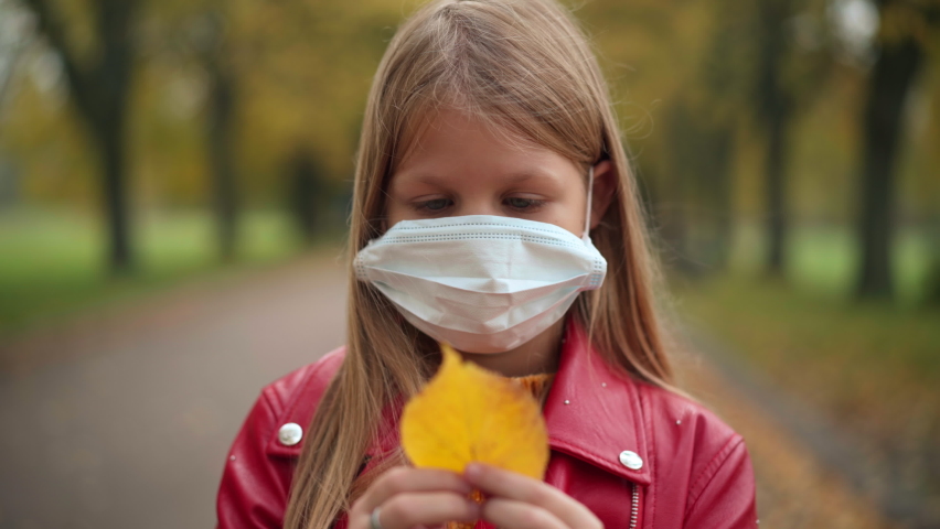 Close-up charming frustrated teen girl in Covid face mask with yellow autumn leaf looking at camera with sad facial expression. Headshot portrait of depressed Caucasian teenager posing on pandemic | Shutterstock HD Video #1094635427