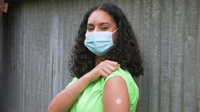 Beautiful biracial African American teenager young woman outside wearing a face mask and showing her vaccine sticking plaster and giving thumbs up during COVID-19 Coronavirus pandemic - Powered by Shutterstock - Get 15% off with code: PIKWIZARD15