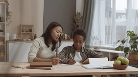 Chest up of loving Biracial mother kissing on cheek ten-year-old African American son sitting by desk at home doing homework, writing on paper - Powered by Shutterstock - Get 15% off with code: PIKWIZARD15