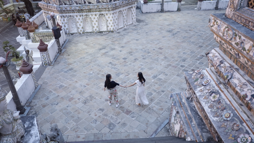 Female friends hold hands and walk around Buddhist temple in Asia