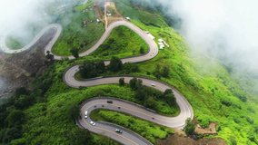 Aerial video top view drone road photo over green mountains with white fog floating and paths exciting steep road way of travel.