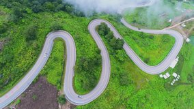 Aerial video top view drone road photo over green mountains with white fog floating and paths exciting steep road way of travel.