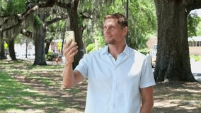 Portrait of  handsome man holding smartphone. Guy walking and having video call in city park.
