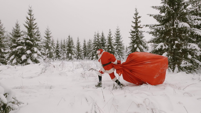 Funny video of Santa Claus having fun running gallop with huge bag of gifts in winter forest. Delivery of Christmas or New Year gifts to people.