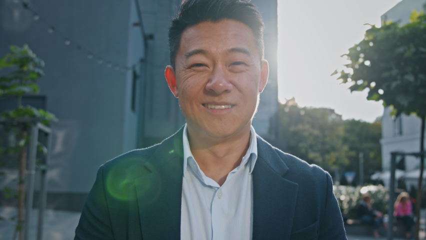 Front view portrait smiling happy Asian middle-aged businessman Korean adult entrepreneur employer man worker manager investor architect standing in city outdoors posing in sun lights sunbeams sunset Royalty-Free Stock Footage #1094657235