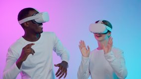 Multiethnic couple in vr goggles and white clothes dance isolated over neon background. African-American man and caucasian woman dancing in augmented reality glasses