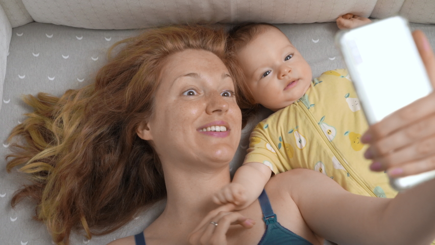 Young mother and her newborn baby making a selfie or video call in a bed. Technology, family, parenthood. Top view