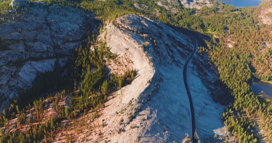 Highway built in the middle of a curvy mountain. Green pine tree forest growing at the foot of the rocks. Aerial view.