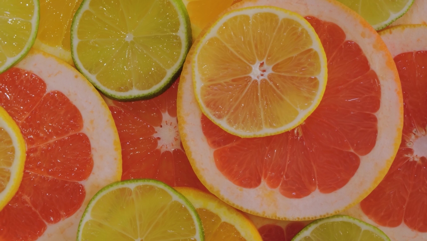 Top view: many colorful fresh citrus orange, grapefruit, lemon and lime fruit slices on slow rotating surface - close up. Summer, tropical, natural, exotic and healthy food concept | Shutterstock HD Video #1094666621