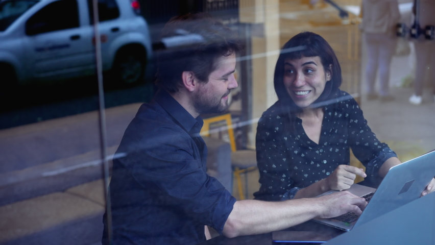 Happy millennials discussing work in front of laptop in urban workplace. Youg man and woman colleagues working and laughing