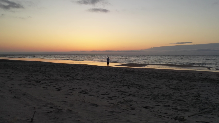 Solitary walker on beach beside ocean waves at sunrise while on family vacation in coastal South Carolina