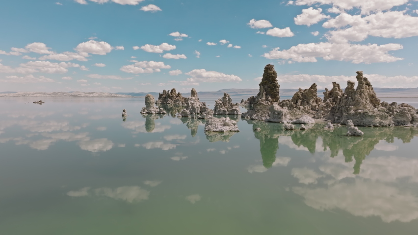 Tall spires along the shoreline of ancient Mono Lake. Aerial view of unique mineral rock formations below bluish skyline reflecting on water surface. High quality 4k footage