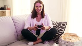 Beautiful excited young gamer girl sitting on a couch and playing in video games on a console. Happy player woman controlling joystick for videogame.
