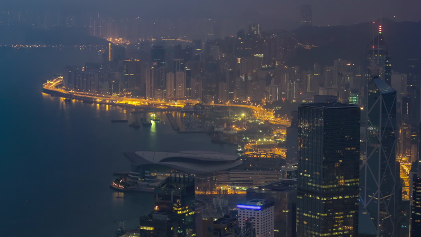 The famous foggy view of Hong Kong from night to day transition aerial timelapse from Victoria Peak. Taken before sunrise with colorful clouds over Kowloon Bay.