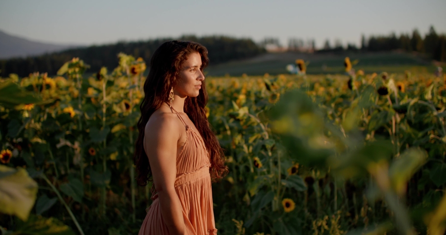 Beautiful joyful girl walking through a sunflower field at sunset, wearing a dress