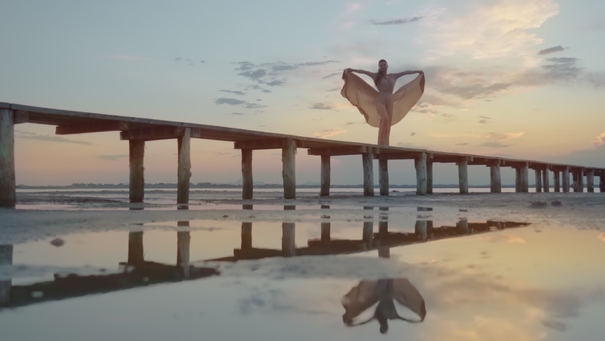 Beautiful sunset on the wooden pier of the beach with fashion model in elegant dress above