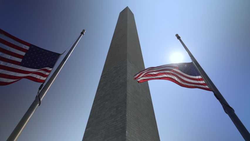 Slow motion camera moving around american flags flying outdoors in bright sun around the Washington Monument in Washington, DC, USA Royalty-Free Stock Footage #1094679889