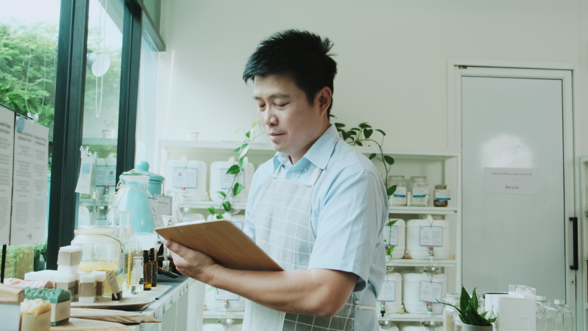 Portrait of Asian male shopkeeper smiles and looks at camera, arms crossed at refill store, natural products, zero-waste grocery, and plastic-free, eco environment-friendly, sustainable lifestyles.