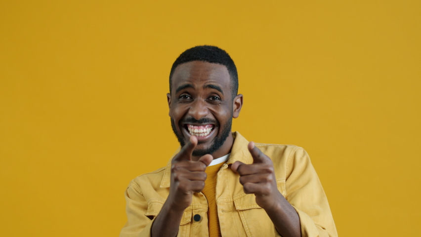 Portrait of overjoyed young Afican American man laughing and pointing at camera on yellow color background. People and positivity concept. | Shutterstock HD Video #1094684065