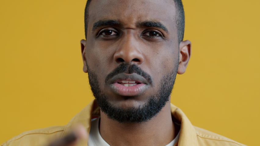 Close-up portrait of violent Afican American man yelling and pointing at camera on yellow background. Negative emotions and people concept. | Shutterstock HD Video #1094684087