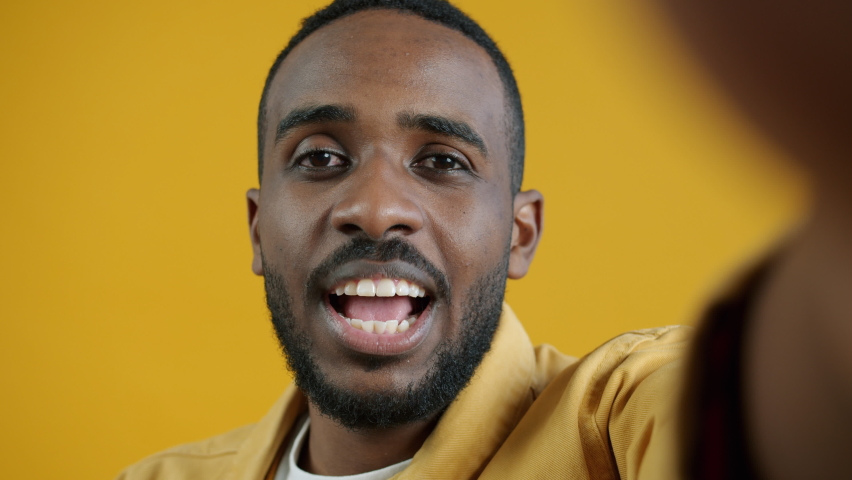 Close-up portrait of handsome Afican American guy talking looking at camera during video call on yellow color background. People and communication concept. | Shutterstock HD Video #1094684097