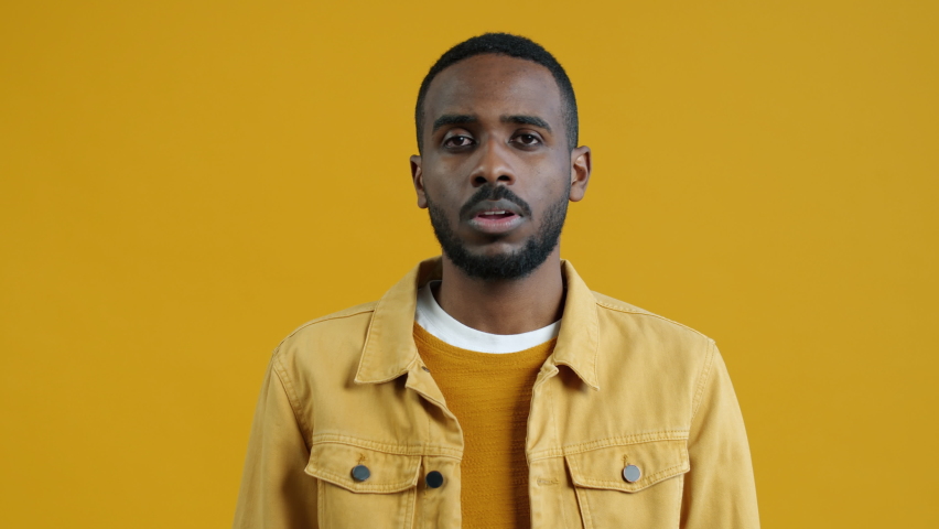 Portrait of confused young Afican American man staring at camera making binoculars hand gesture on yellow color background. People and expressions concept. | Shutterstock HD Video #1094684105