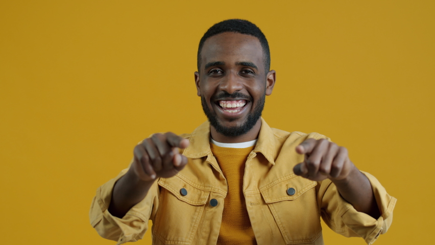 Slow motion portrait of good-looking young Afican American man making heart hand gesture and smiling looking at camera on yellow background | Shutterstock HD Video #1094684109