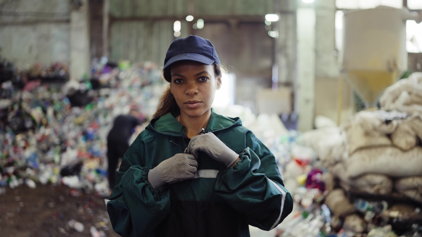 Portrait of a young African American woman at a recycling plant. Garbage in the background. Pollution control | Shutterstock HD Video #1094690253
