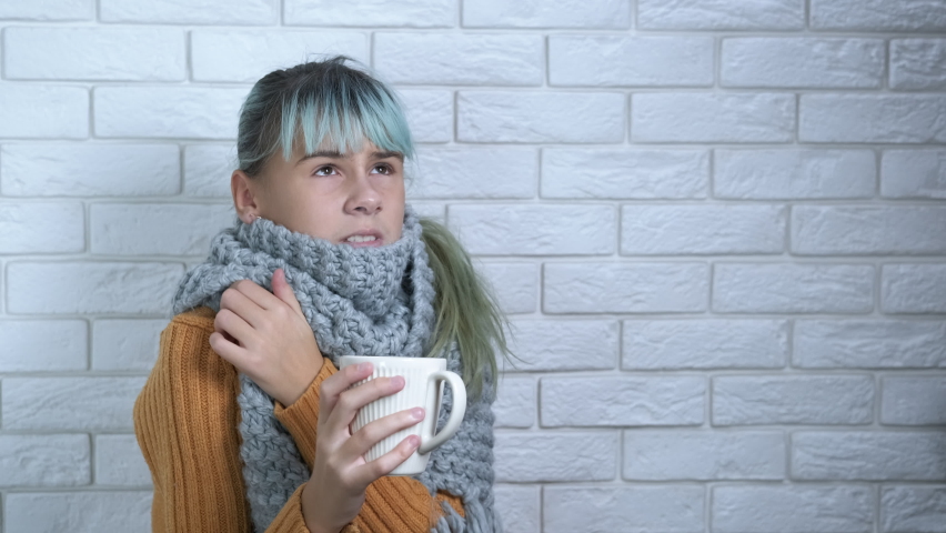 Child in unheated room. An unhappy child get warm with hot cup of tea and woolen scarf in unheated room during economical and energy crisis.