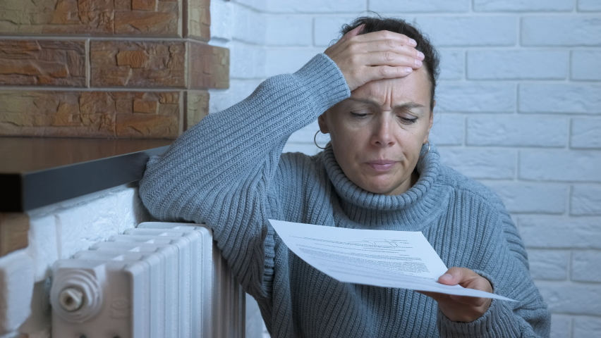 High bills for heating system. A woman sits by heating system in warm woolen clothes with domestic bills in the room. A concept of high heating bills in Europe. Royalty-Free Stock Footage #1094691017