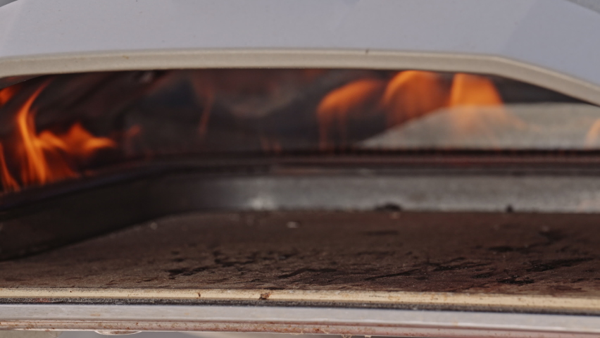 Lockdown Medium Slow Motion Shot Of Man Using Pizza Paddle To Put Pizza Into Mini Pizza Oven, Outdoors