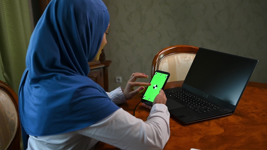 Rear view of a Muslim woman in hijab, talking during an online conference, using her modern smartphone with green chromakey screen with copy advertising space. Ideal video for insert promotional clip | Shutterstock HD Video #1094694853
