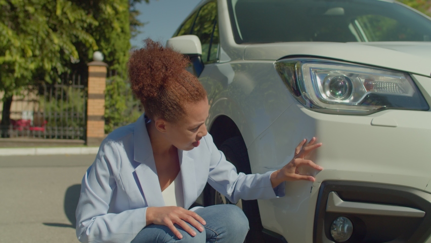 Frustrated upset lovely African American woman driver sitting near parked vehicle on roadside, checking car scratches and dents after accident while driving car in city on business trip. . | Shutterstock HD Video #1094695069