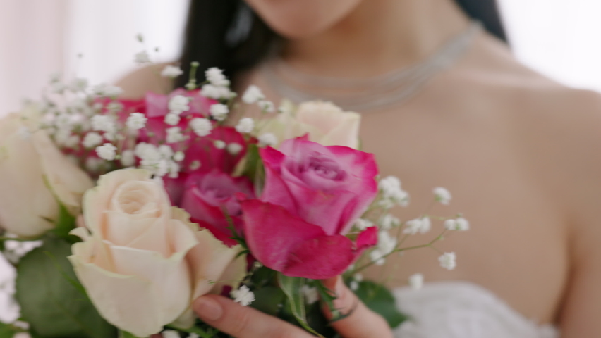 Happy, smile and asian bride with flowers in wedding dress at marriage, reception or celebration. Joyful, excited and nervous bride smelling pink and white bouquet on wedding day with happiness.