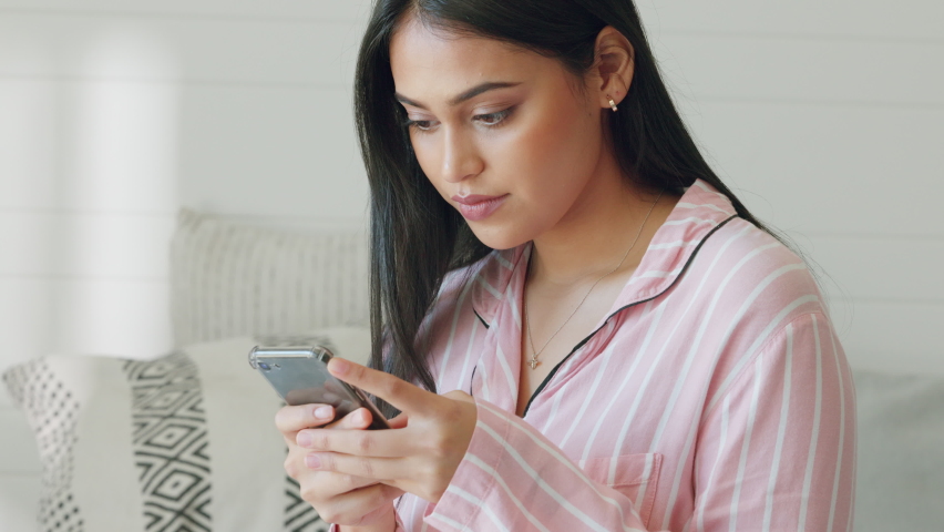 A young, smile and happy woman getting notification on smartphone while sitting on couch in her home. Excited lady has phone in hands with positive news, text or message sitting on sofa in lounge. | Shutterstock HD Video #1094698177