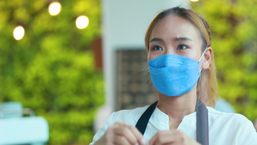 Asian female owner small business wearing protective face mask turning open sign banner. | Shutterstock HD Video #1094699579