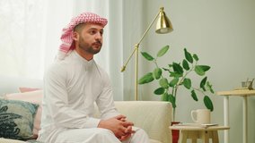 Middle eastern man watching tv close-up. Male person watches television in living room. Wearing traditional Islamic clothes, relaxing at home.