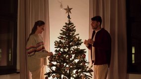 winter holidays and people concept - happy couple decorating christmas tree at home in evening - Powered by Shutterstock - Get 15% off with code: PIKWIZARD15
