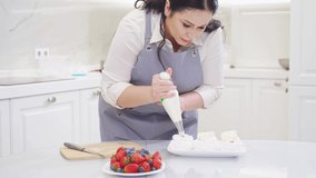 a female chef adds cream from a pastry bag to Anna Pavlova cakes in the kitchen. recipes for delicious traditional desserts. cooking school and courses. Record video and photo lessons.