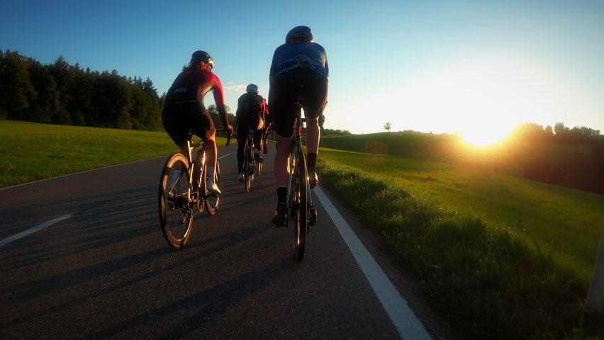 Group of professional cyclists riding bicycles at sunset. Friends on road bikes riding at countryside with green hills and mountains at sunrise. Cycling concept