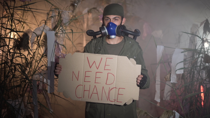 A man in a gas mask holding poster with words We Need Change. burning plastic trash on the background. environmental problems: plastic garbage, illegal dumps, waste incineration | Shutterstock HD Video #1094712767