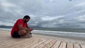 man sitting on wooden deck in front of the beach using his phone, young man in video conference in front of the sea